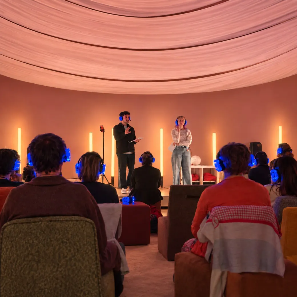Deelnemers met koptelefoon en twee presenters tijdens The Energy Reset in een sfeervolle ronde ruimte